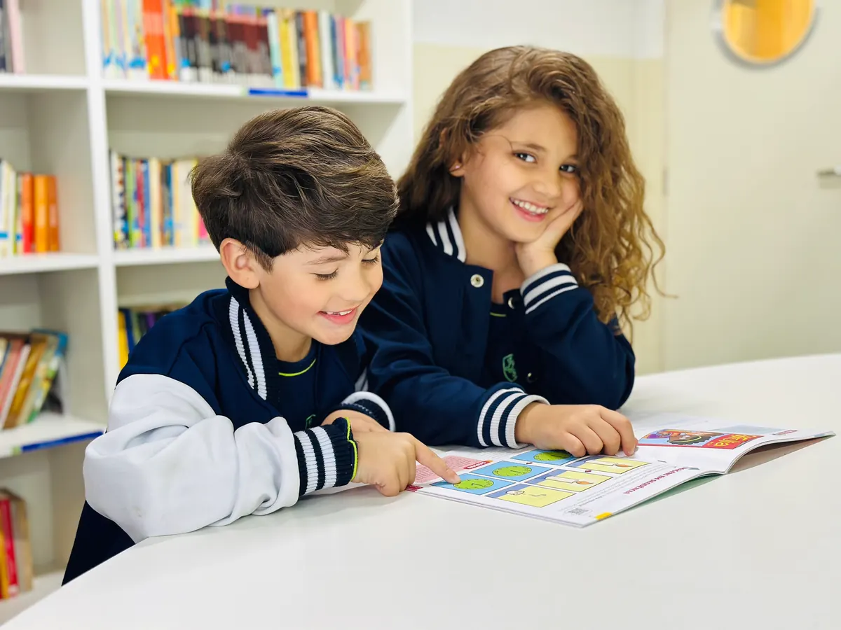 Duas crianças do colégio explorando uma atividade em livro na biblioteca