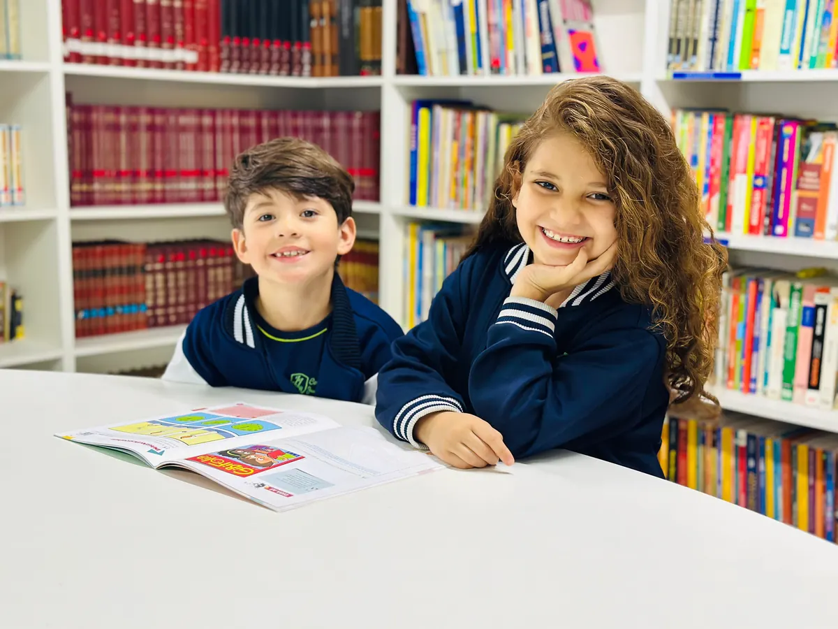 Dois estudantes do colégio sentados juntos na biblioteca com material de estudo