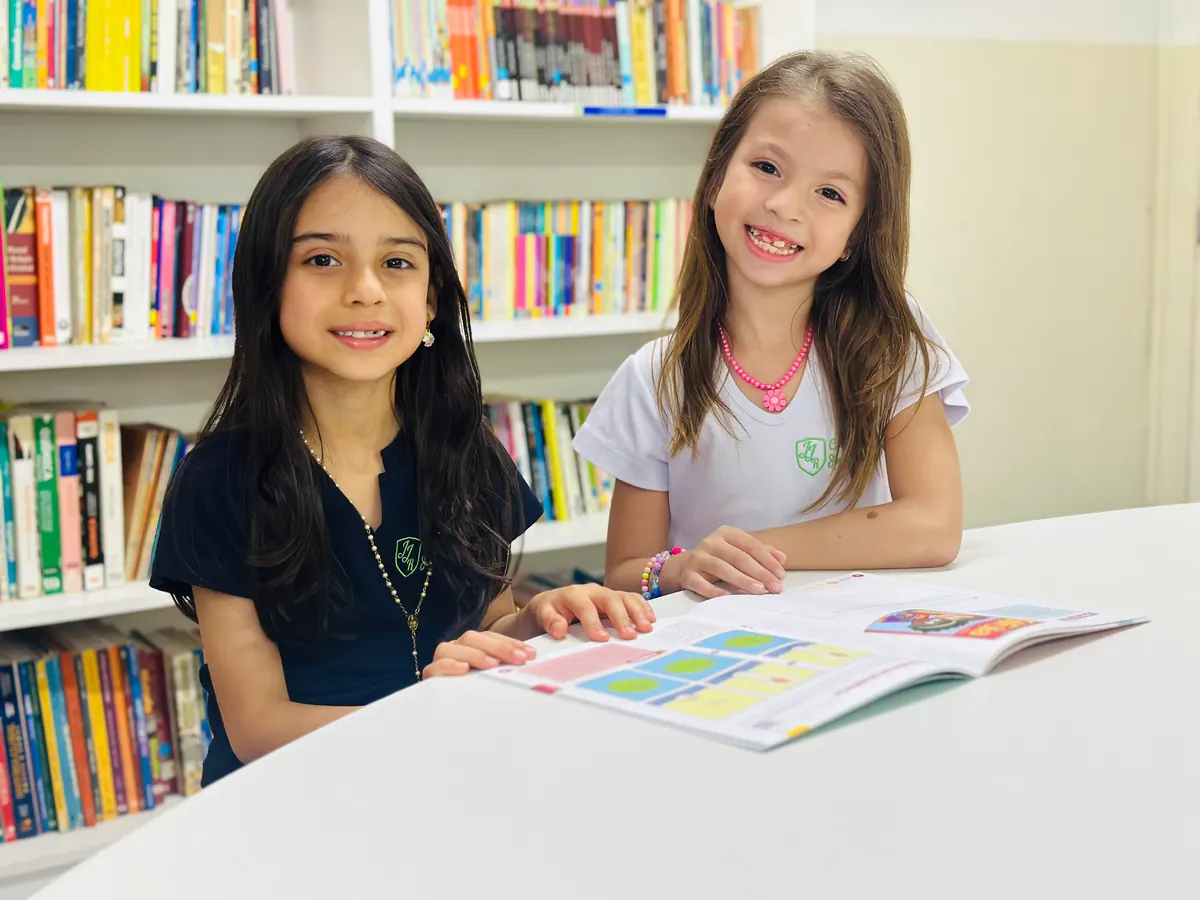 Duas estudantes do colégio reunidas com material de estudo na biblioteca