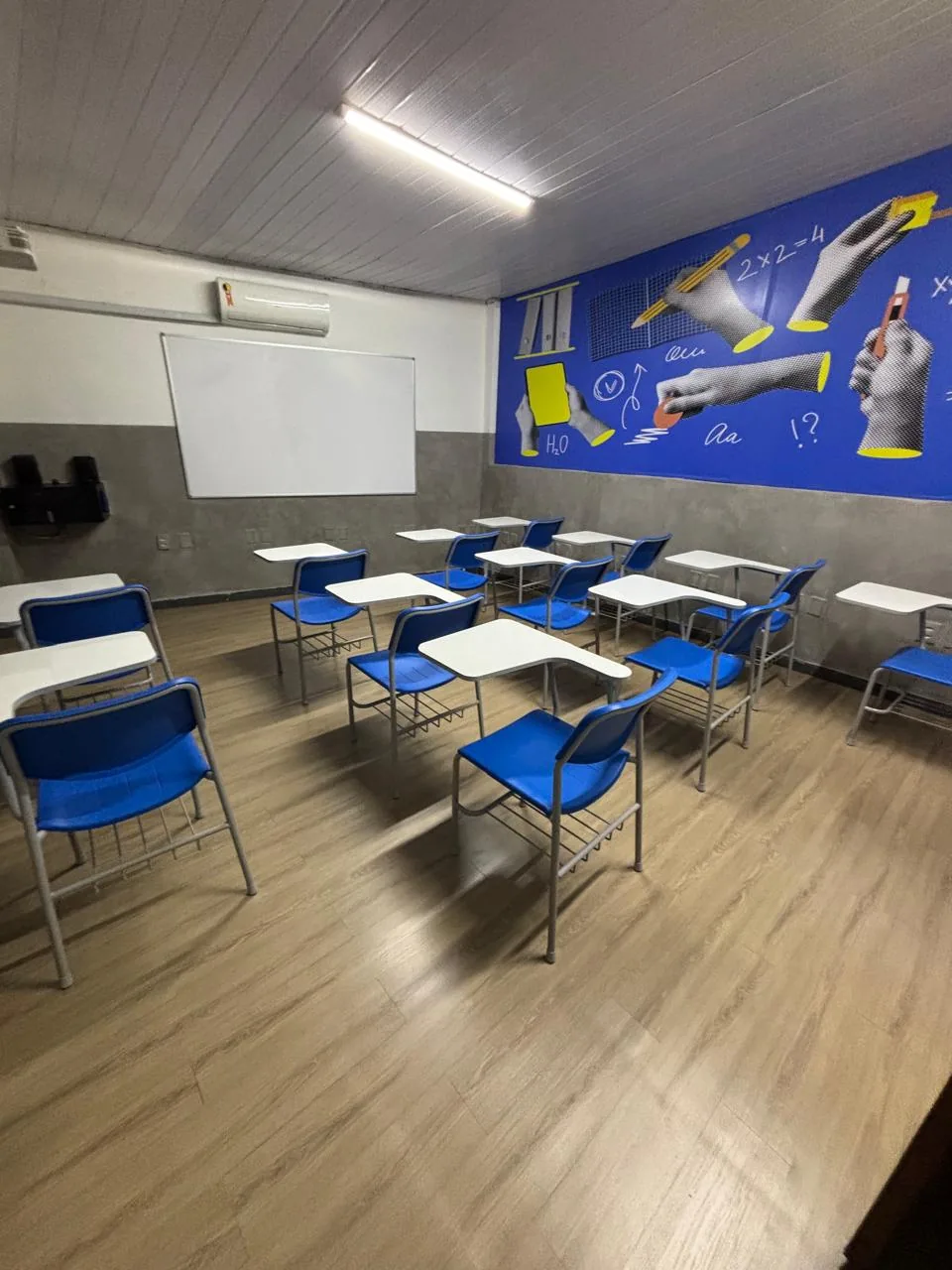 Sala de aula do Colégio JJR com carteiras, lousa e mural azul